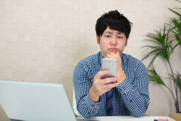 スマホ画面を見ながら悩む男性