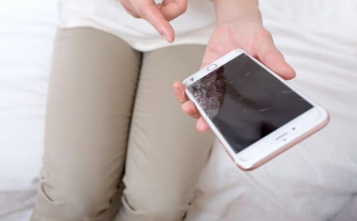 割れたスマホ画面を指さす