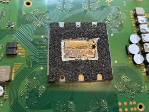PS5の緑色の基板上にあるAPU(メインチップ)。周囲を黒いスポンジで囲まれ、表面の液体金属が劣化してムラになっている状態。