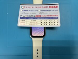 バッテリー交換が完了し、正常に起動・表示テストを行っているApple Watch Series 3。画面の上部には「スマホスピタル総合病院 診察券」のカードが置かれており、修理が成功して復活した様子。